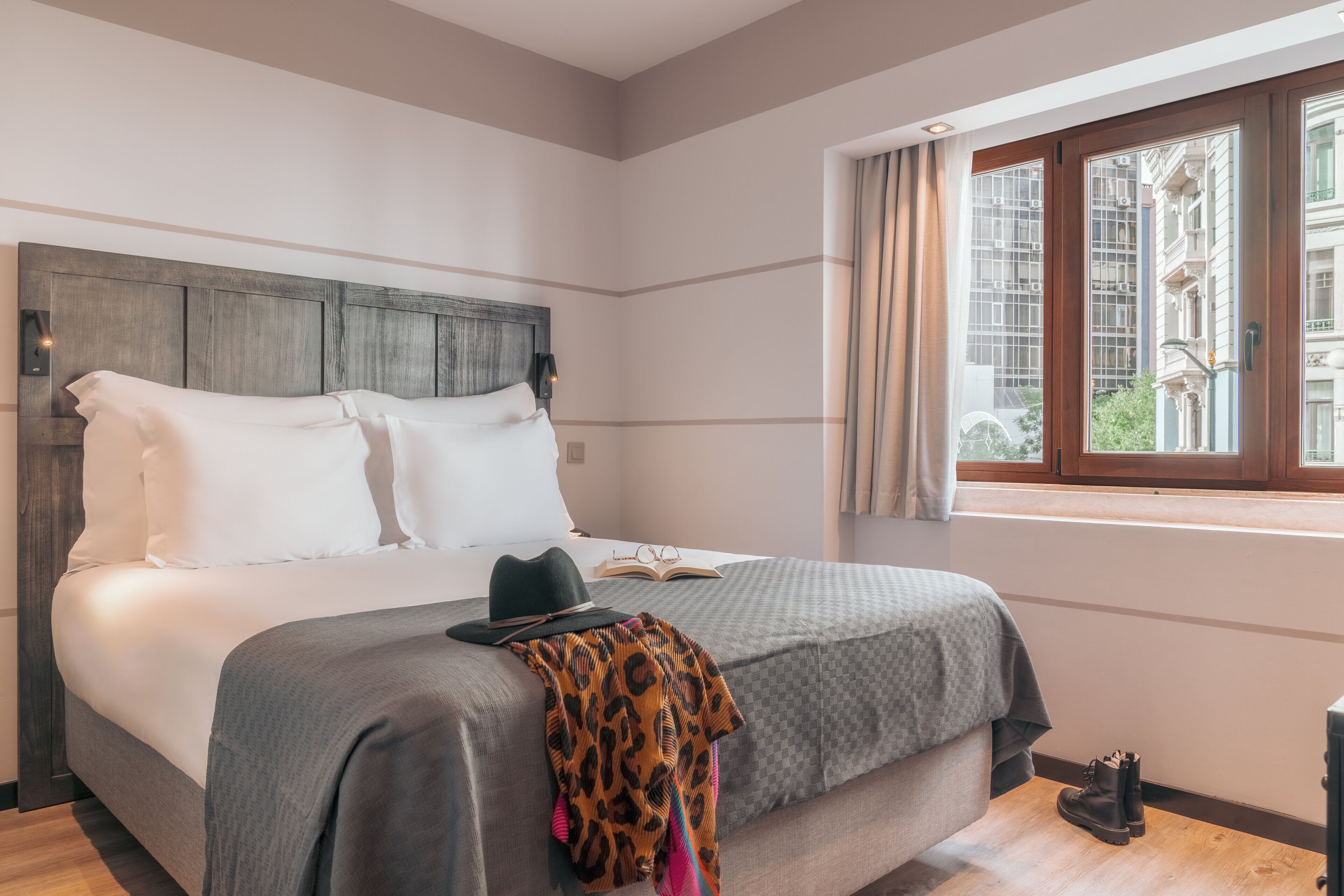 A neatly made bed with a grey blanket, a black hat, and a leopard print throw on the foot of the bed.