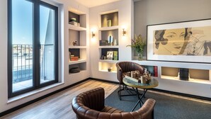 A modern living room with a large window, built-in shelves, a leather armchair, and a small round table. - Pestana Lisboa Vintage City Center Suites (Lisbon)