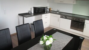 A modern kitchen with a dining table, chairs, a microwave, a coffee maker, and an oven. - Apartment right on the Dutch border (Oeding)
