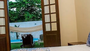 Un dormitorio con cama, vista a una piscina y zona exterior a través de una puerta abierta.