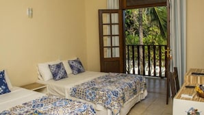 Una habitación con dos camas, una puerta de madera y vistas al verdor exterior.