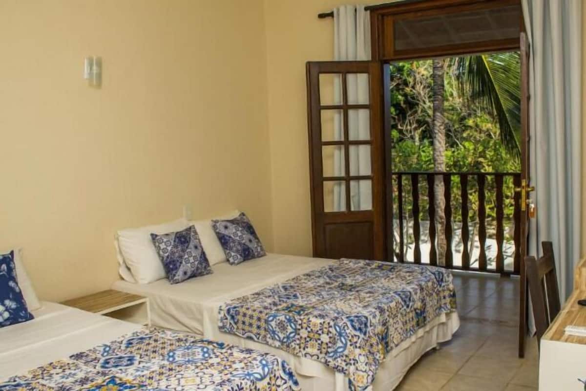 Una habitación con dos camas, una puerta de madera y vistas al verdor exterior.