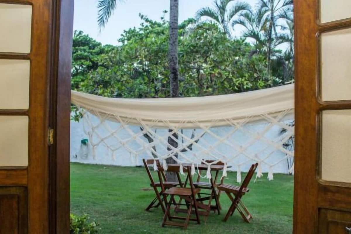 Un área de estar al aire libre con mesa y sillas bajo un toldo blanco, rodeada de abundante vegetación.