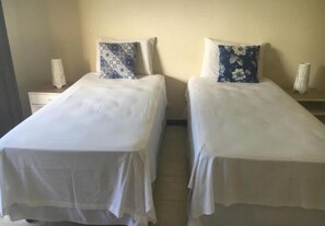 Two single beds with white linens and patterned pillows, a nightstand with a lamp, and a plain wall. - Pousada Trinacria (Salvador)
