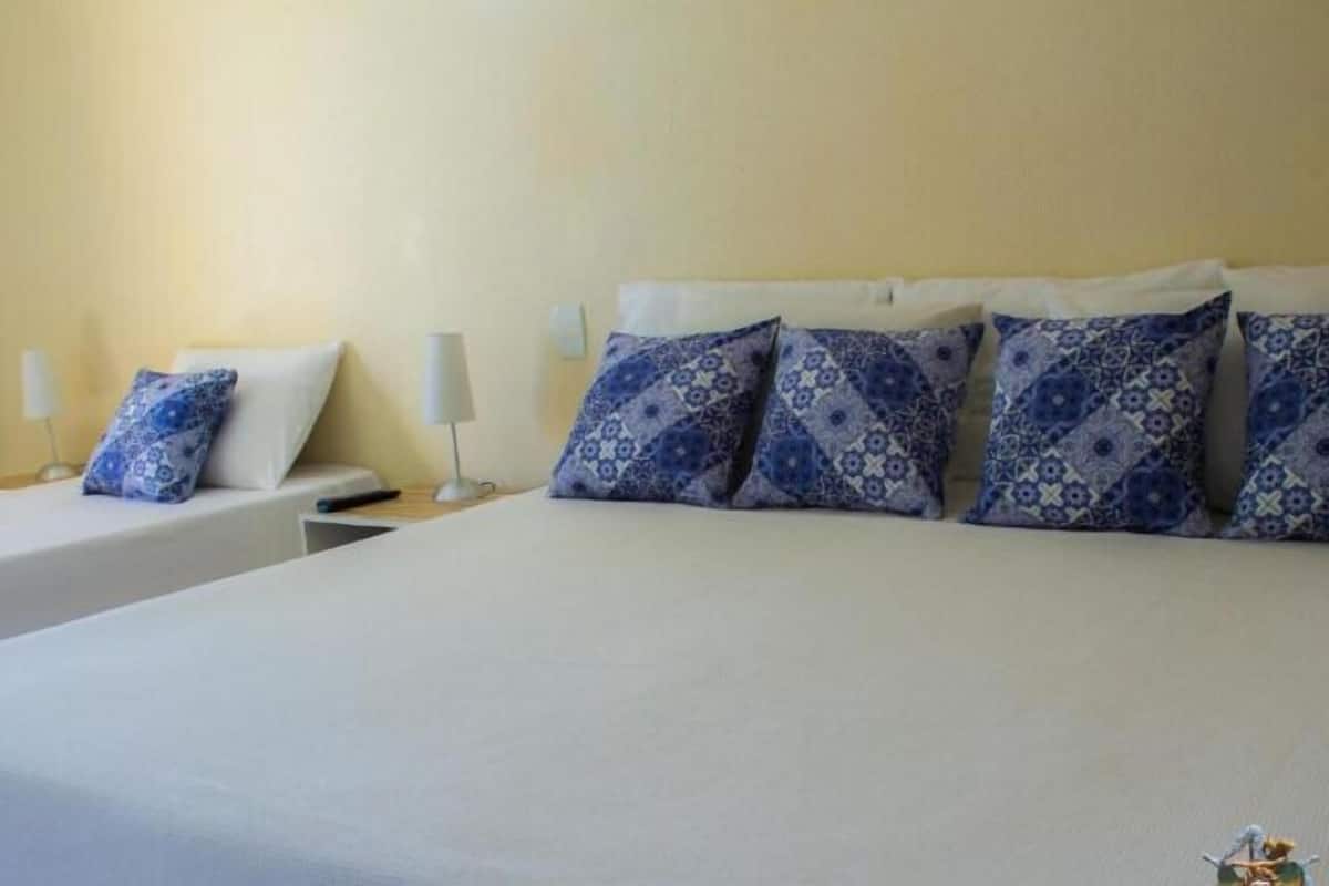 Habitación de hotel con dos camas, cada una con ropa de cama blanca y almohadas azules estampadas. Hay mesitas de noche con lámparas y una pequeña mesa entre las camas.