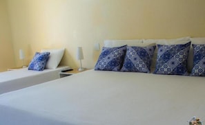 Une chambre d’hôtel avec deux lits, chacun agrémenté de draps blancs et d’oreillers à motifs bleus. On y trouve des tables de chevet avec des lampes, ainsi qu’une petite table placée entre les deux lits.