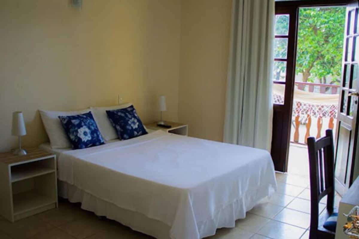 Habitación de hotel con cama, dos mesitas de noche y vistas al balcón exterior.