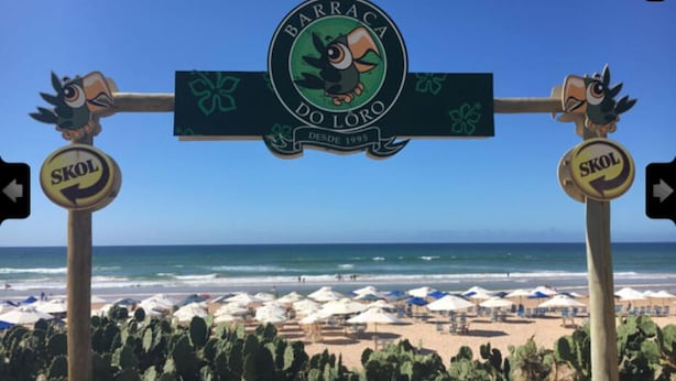 Un cartel frente a la playa con un logotipo y el texto 'BARRACA DO LORO' y 'SKOL', que indica una zona de playa.