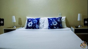 Una cama con ropa blanca y dos almohadas azules con estampado floral, flanqueada por mesitas de noche con lámparas.