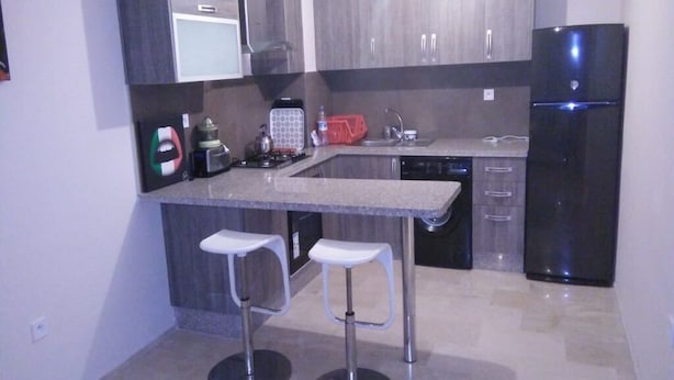 A modern kitchen with grey cabinets, a black refrigerator, a built-in oven, and two white bar stools. - Furnished apartment in Marrakech AT10 (Marrakech)