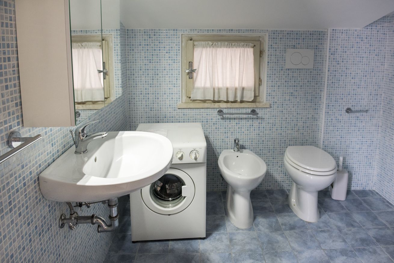 Ein Badezimmer mit Waschbecken, Waschmaschine, Bidet, Toilette und einem Fenster mit Vorhang.