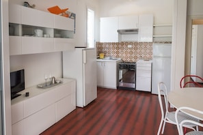 A compact kitchen with white cabinets, a stove, and a dining area with a table and chairs. - M104 - Marcelli, villa with garden 200 meters from the sea (Marcelli)