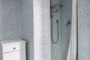 Une salle de bain avec une douche, des murs carrelés et un meuble blanc.