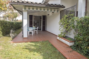 Une terrasse couverte avec une table et des chaises, un sol carrelé et une vue sur l’intérieur de la maison.