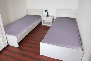 Une petite pièce avec deux lits simples, une table de chevet avec une lampe et un sol carrelé.