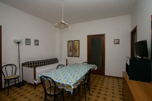 A room with a dining table, chairs, a bench, a television, and a patterned floor.