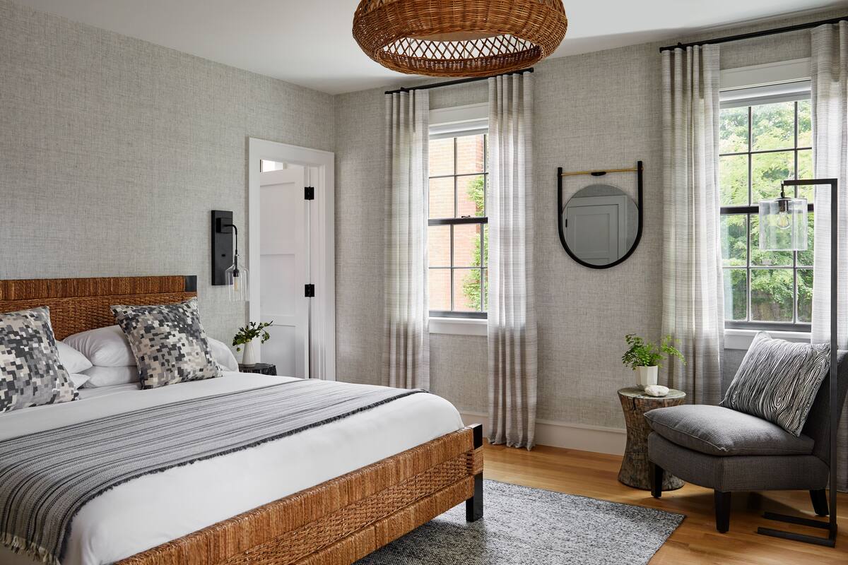 A bedroom with a large bed, a side table with a plant, a chair, and a window with curtains.