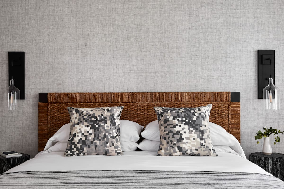 A neatly made bed with a wooden headboard, two patterned pillows, and a bedside table with a vase of flowers.