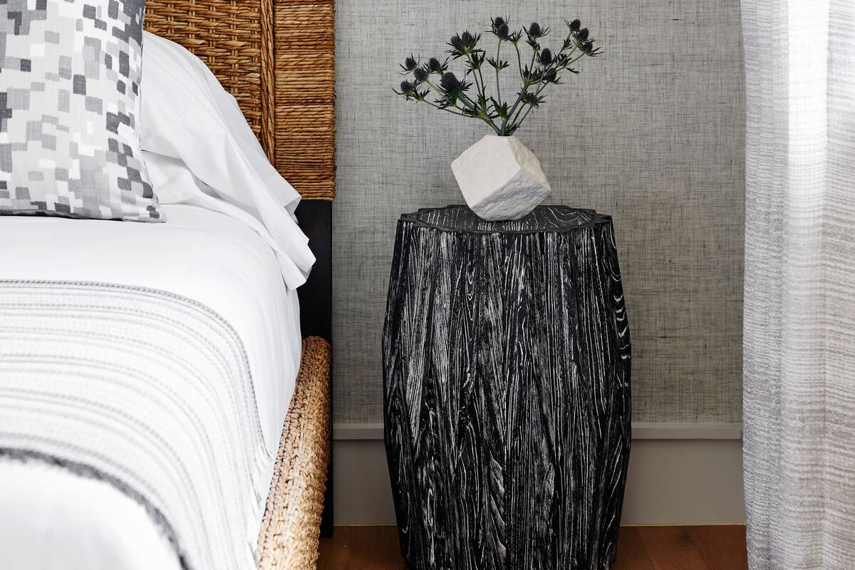 A neatly arranged bedroom with a bed, a side table with a vase, and a wall-mounted light fixture.