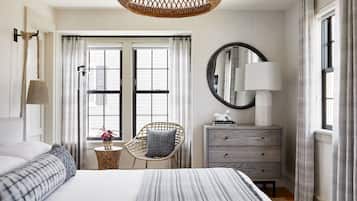 A hotel room with a large bed, a wicker chair, a dresser, and a window with curtains.