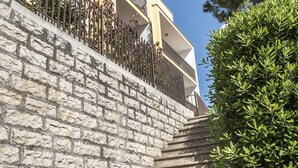 Escadaria de pedra que leva a um edifício com varanda, cercada por vegetação.