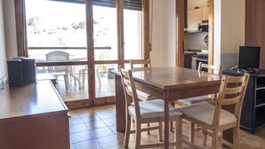 Uma sala de jantar com mesa e cadeiras de madeira, uma cozinha ao fundo e vista através de uma porta de vidro.