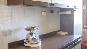 Uma cozinha com eletrodoméstico de aço inoxidável na bancada, painel de azulejos e um armário acima.
