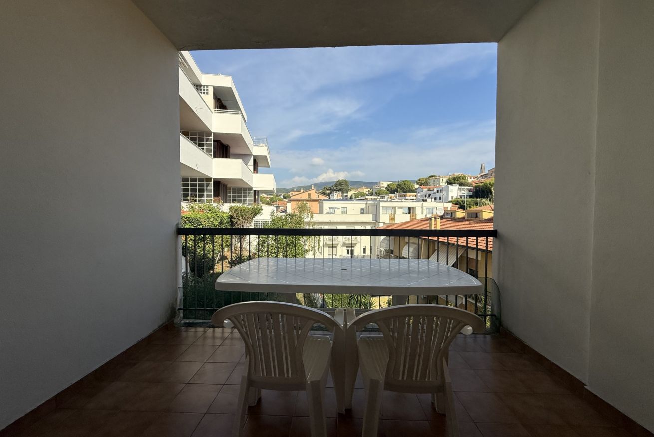 A balcony with a table and chairs, overlooking a residential area with buildings and a clear sky.