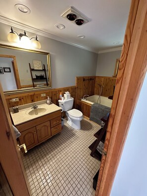 Une salle de bain avec un lavabo, des toilettes et une baignoire, des panneaux de bois et un grand miroir.