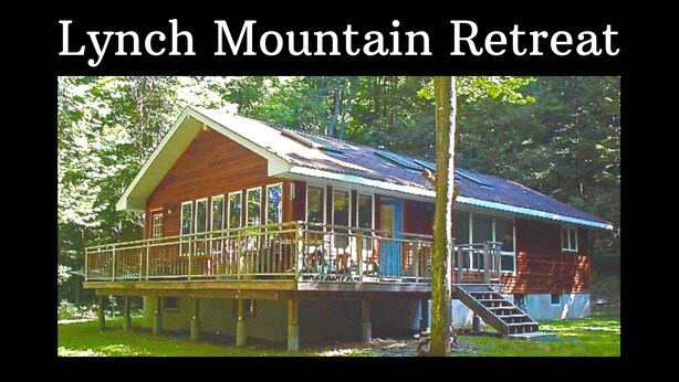 A wooden cabin with a porch and stairs leading to a deck, surrounded by trees. - Lynch Mountain Retreat (Cooperstown)