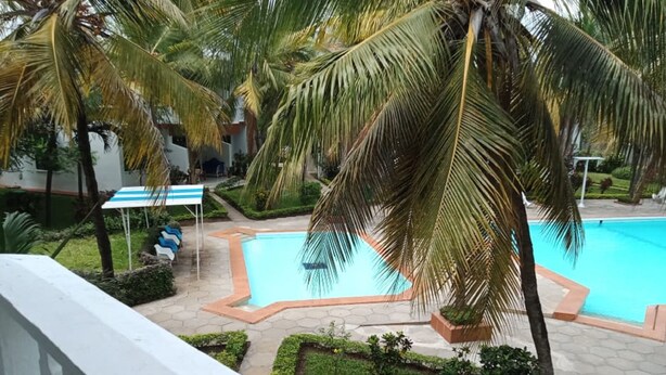 A swimming pool surrounded by palm trees and a small garden area. - 3 Bedroom Apartment In Nyali (Mombasa)