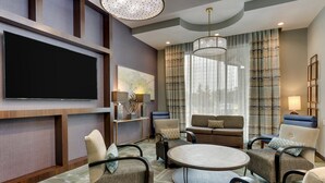 Un salon moderne doté d’un téléviseur à écran plat, de sièges confortables, d’une table basse ronde et d’une grande fenêtre avec des rideaux.