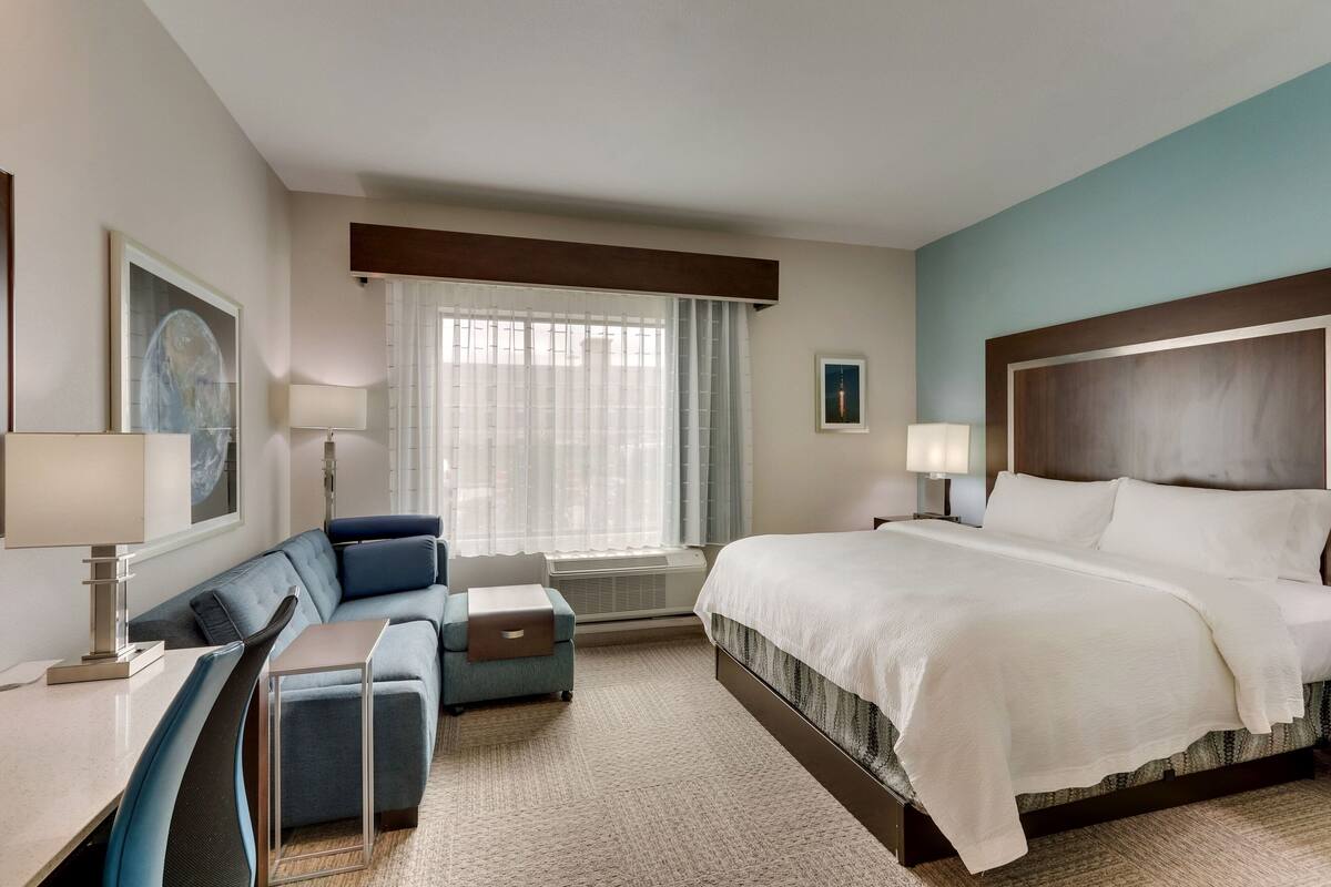 Une chambre d’hôtel avec un grand lit, un canapé, un bureau et une fenêtre avec des rideaux.