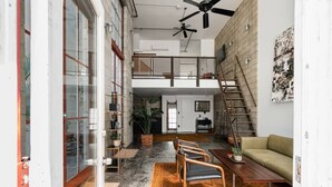 Un loft spacieux avec une mezzanine, un escalier et une grande fenêtre donnant sur la ville.