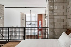 Une chambre à coucher avec un lit, une fenêtre donnant sur un beau paysage, un ventilateur de plafond et un balcon avec une balustrade.