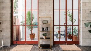 Une pièce avec un mur en briques, une porte à cadre rouge et une étagère ornée de plantes et d’une radio.