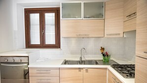 A kitchen with wooden cabinets, a stainless steel sink, a stove, and a window with blinds. - N216 - Numana, sky-earth in the alleys 200mt from the sea (Numana)