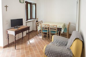 Une pièce comprenant un lit, un bureau avec un ordinateur, une table à manger avec des chaises, une fenêtre et une croix accrochée au mur.