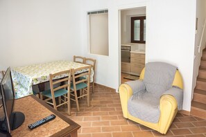 Une pièce comprenant une table à manger, des chaises, un téléviseur, une télécommande, un canapé et un coin cuisine.