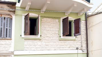 Ein Gebäude mit zwei offenen Fenstern, einer Stein-Fassade und einem weißen Balkon.