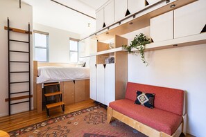A compact room with a bunk bed, a red sofa, a wooden ladder, and a patterned rug. - Room T at The Dutra Inn - Little Italy (San Diego)