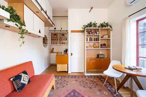 A compact living space with a sofa, a dining table, a kitchen area, and a bookshelf. - Room T at The Dutra Inn - Little Italy (San Diego)