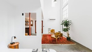 Ein modernes, helles Zimmer mit einem großen Fenster, einem roten Teppich mit Muster und einer Zimmerpflanze.