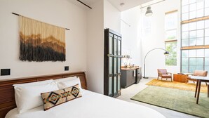 Et hotelværelse med en stor seng, et tekøkken, et spiseområde med stole og udsigt gennem store vinduer.