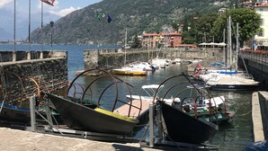 A harbor with boats docked, a lighthouse, and buildings in the background. - Lake Sunset View - Como Lake (Bellano)