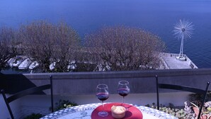 A table with two wine glasses and a bowl of bread, overlooking a lake with mountains in the background. - Lake Sunset View - Como Lake (Bellano)