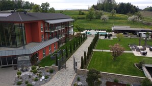 Um hotel moderno com fachada vermelha, piscina e um jardim bem cuidado.