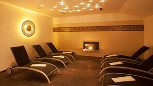 Um quarto com seis poltronas reclináveis dispostas em duas fileiras, uma lareira na parede e um teto com luzes em formato de estrela.