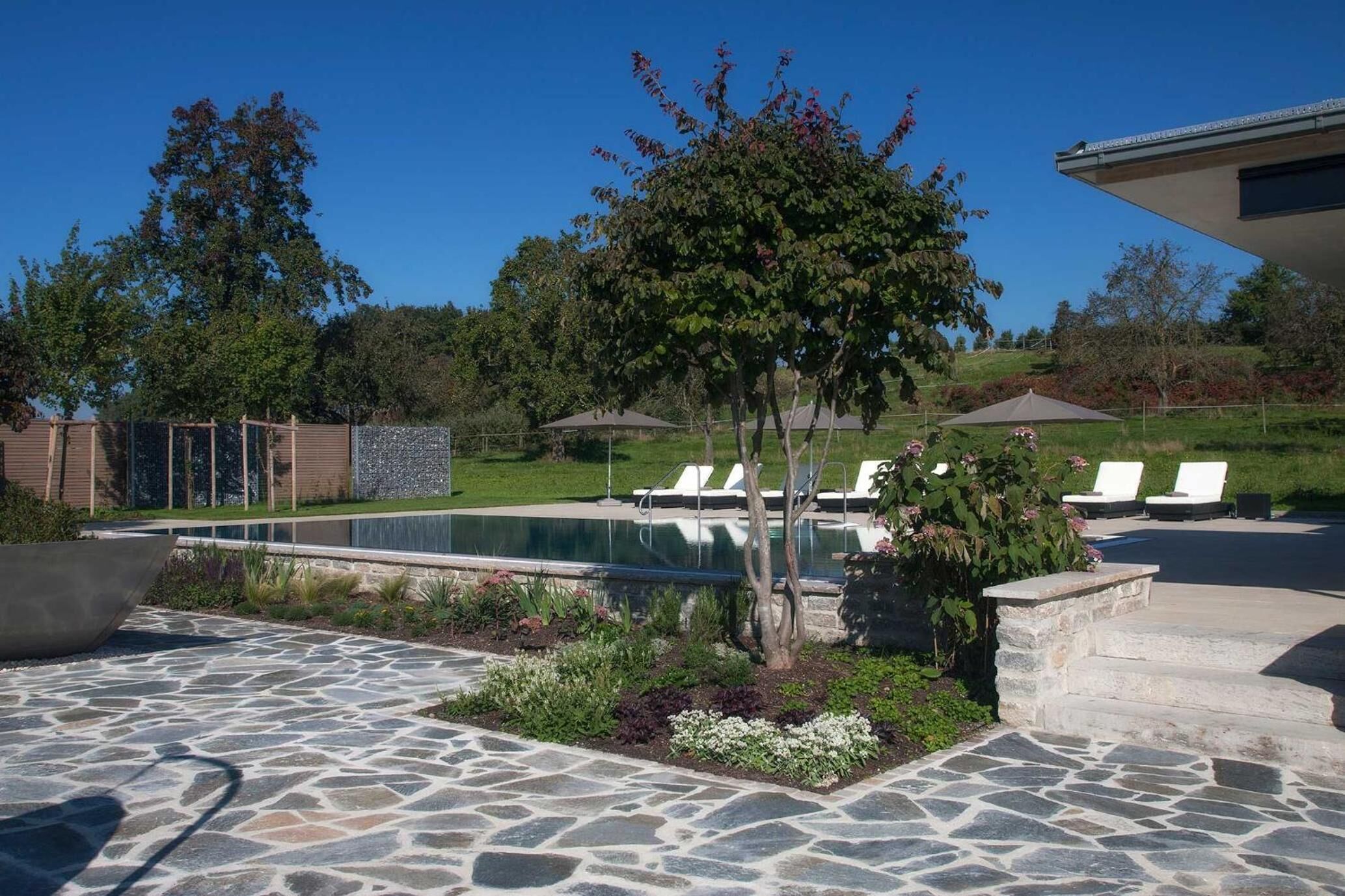 A swimming pool with lounge chairs, a stone patio, and a landscaped garden area.