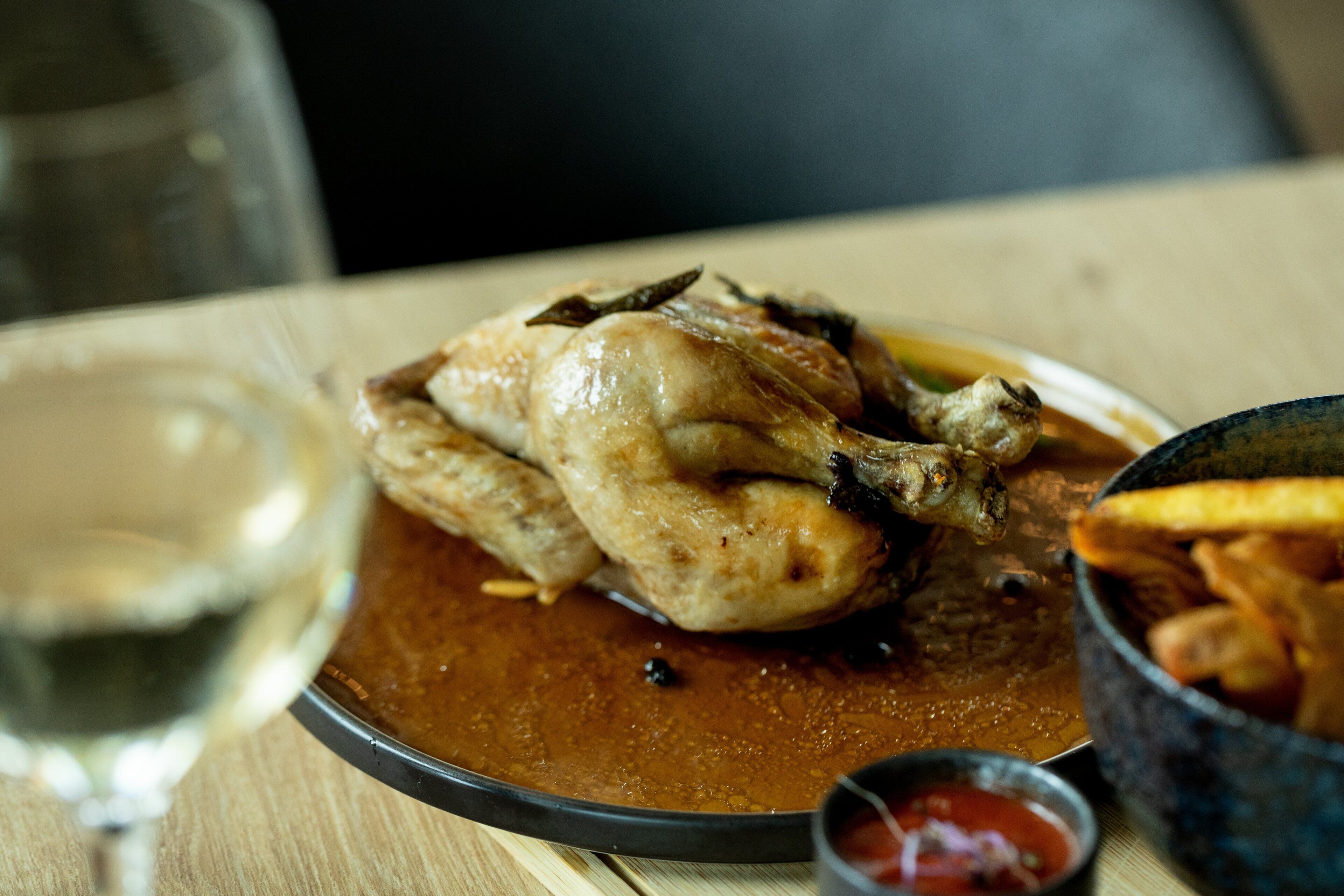 Un piatto con un coscia di pollo arrosto, un bicchiere di vino bianco e una ciotola di patatine fritte.